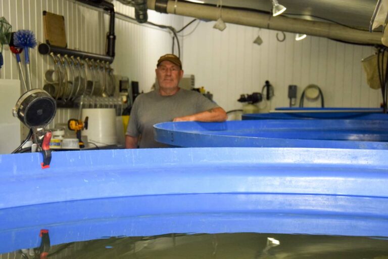 Renaissance man John Caselton stands behind one of a number of large tanks of his own design. The tanks use a solid knowledge of hydrodynamics to filter out solids and send them on to a biofiltering process that returns clean water in the closed system operation. photo by Michael Erskine